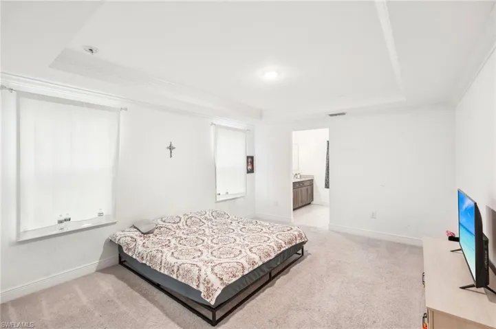 Bedroom with visible vents, light carpet, a raised ceiling, crown molding, and baseboards