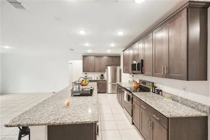 Kitchen featuring light tile patterned floors, visible vents, a kitchen island, dark brown cabinetry, and appliances with stainless steel finishes