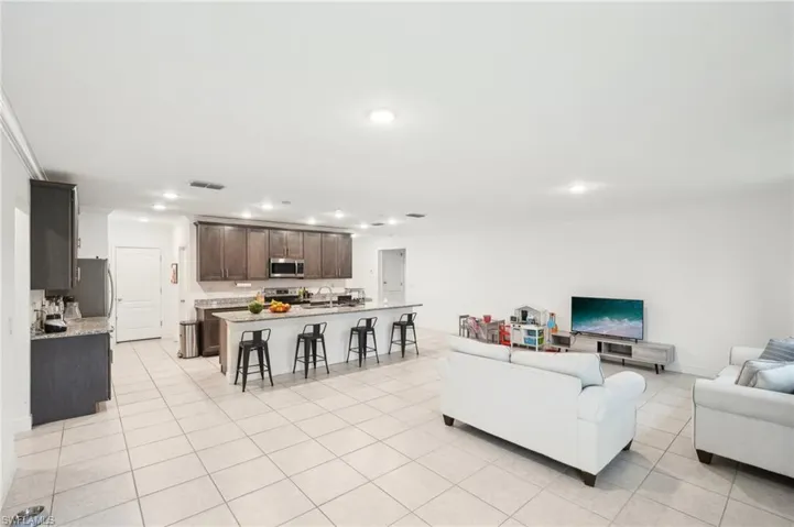 Living room with light tile patterned floors, visible vents, baseboards, recessed lighting, and ornamental molding