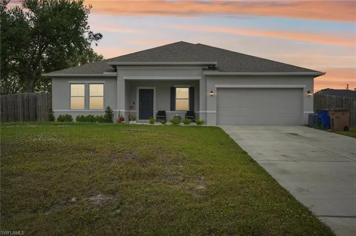 View of front of home with stucco siding, driveway, fence, a front yard, and a garage