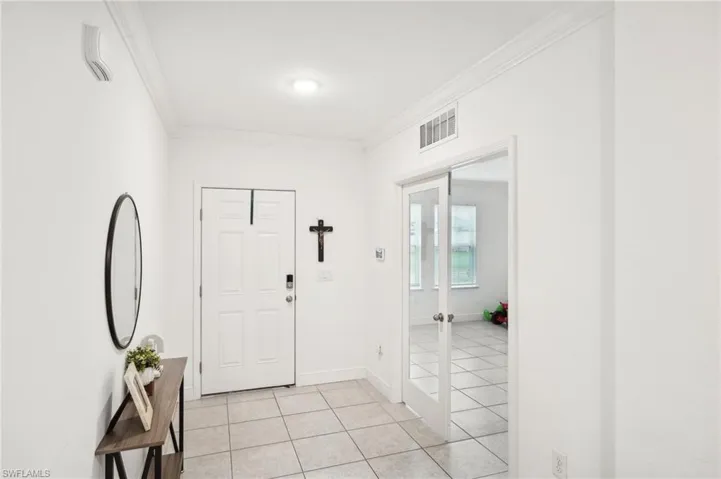 Entrance foyer with light tile patterned floors, visible vents, crown molding, and baseboards