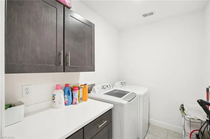 Washroom featuring visible vents, baseboards, light tile patterned floors, washer and dryer, and cabinet space