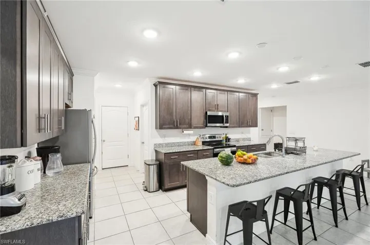 Kitchen with a sink, stainless steel appliances, dark brown cabinetry, a kitchen bar, and crown molding