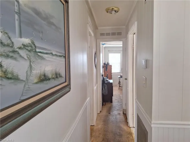 Corridor featuring light wood-style floors, visible vents, ornamental molding, and a decorative wall