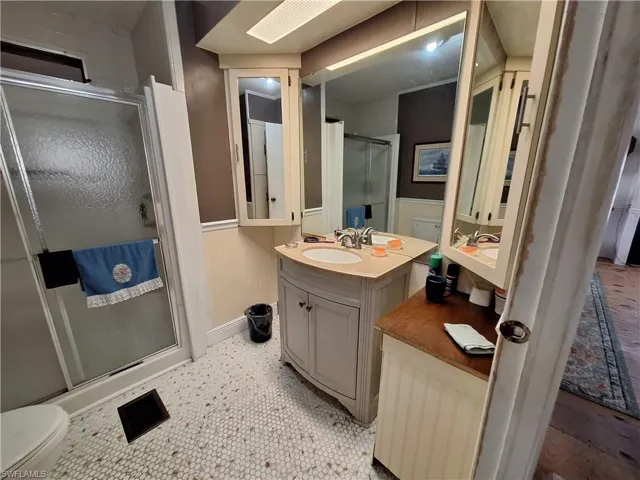 Bathroom with toilet, a stall shower, a wainscoted wall, and vanity