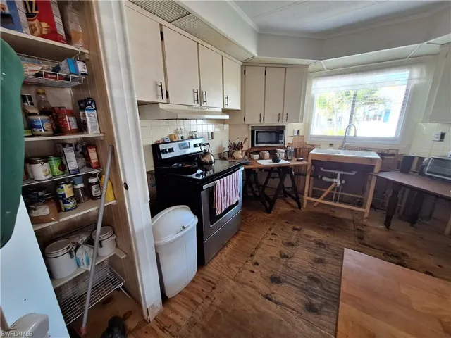 Kitchen with under cabinet range hood, wood finished floors, ornamental molding, stainless steel electric stove, and tasteful backsplash