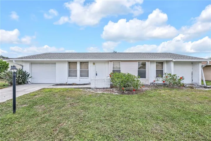 Ranch-style house featuring an attached garage, stucco siding, driveway, and a front lawn