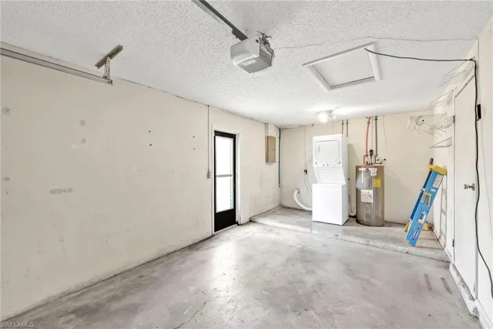Garage featuring stacked washing machine and dryer, electric water heater, a garage door opener, and electric panel