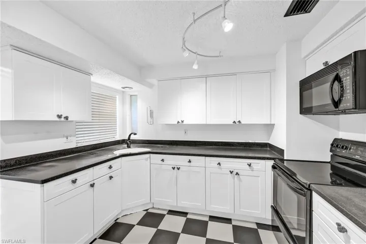 Kitchen with black appliances, tile patterned floors, a sink, white cabinets, and a textured ceiling