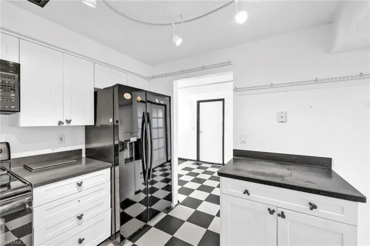 Kitchen featuring tile patterned floors, black appliances, white cabinetry, dark countertops, and a textured ceiling