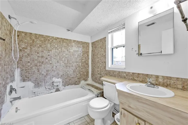 Full bath with a textured ceiling, toilet, bathtub / shower combination, vanity, and tile walls