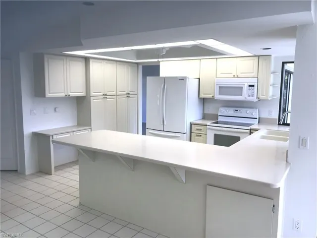 Kitchen with white appliances, light countertops, a peninsula, a kitchen bar, and light tile patterned flooring