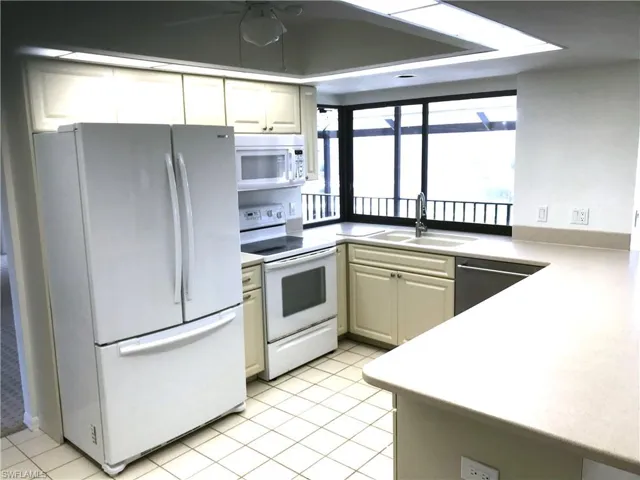 Kitchen with white appliances, light countertops, white cabinets, and ceiling fan