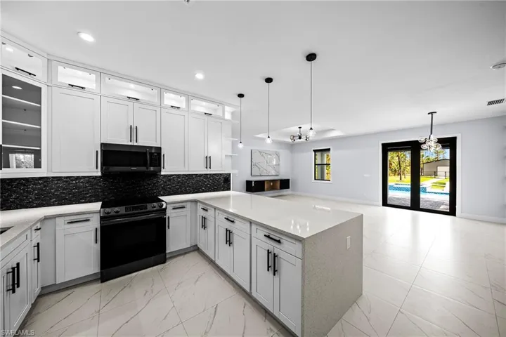 Kitchen with range with electric stovetop, black microwave, light marble finish flooring, a peninsula, and pendant lights