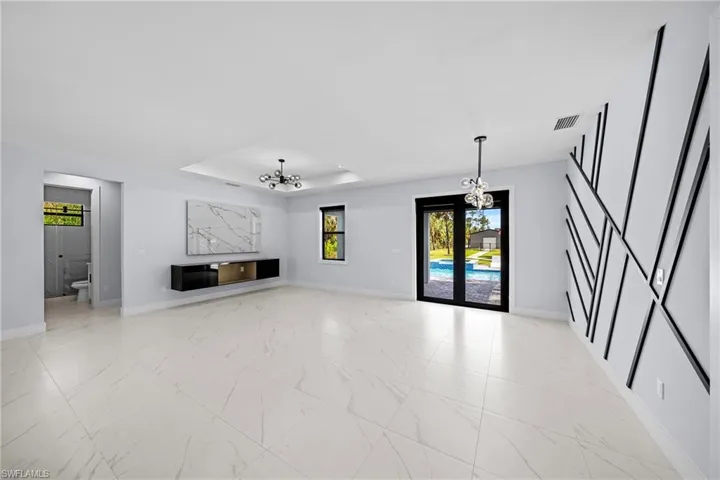 Unfurnished living room featuring a chandelier, light marble finish floors, and baseboards