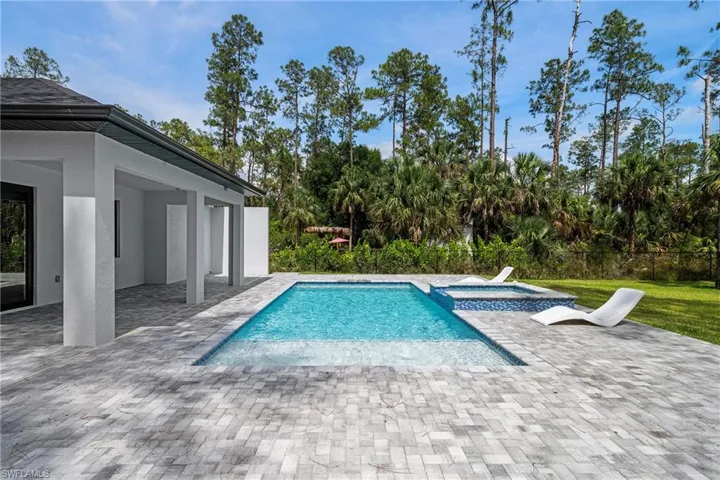 View of pool featuring a patio, a pool with connected hot tub, and view of trees