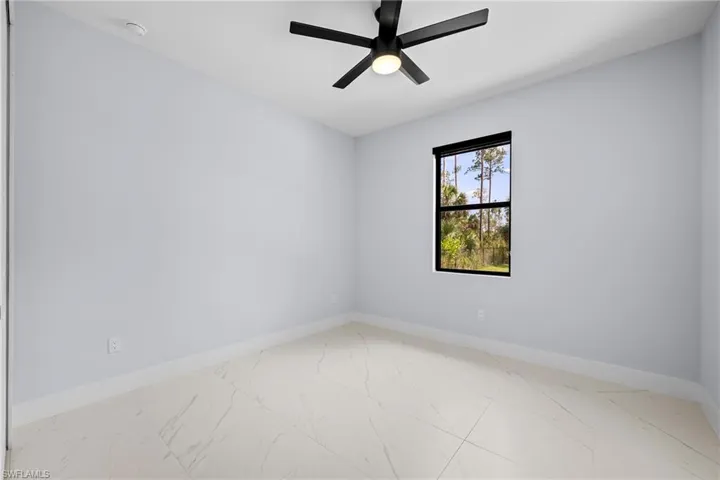 Spare room featuring light marble finish flooring, baseboards, ceiling fan, and a smoke detector