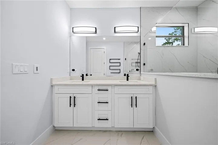 Bathroom with baseboards, a marble finish shower, double vanity, and marble look tile flooring