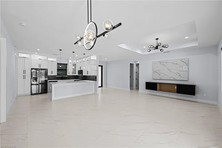 Unfurnished living room featuring a chandelier, light marble finish floors, baseboards, and recessed lighting