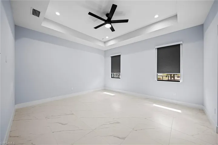 with tray ceiling, light marble finish flooring, ceiling fan, recessed lighting, and baseboards