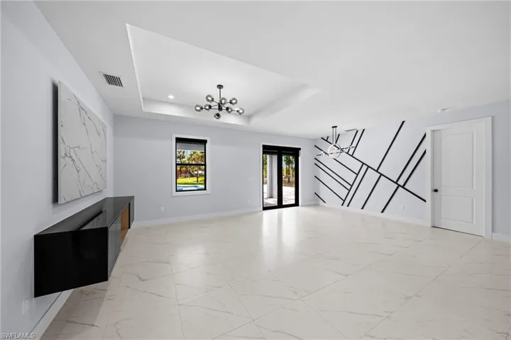 Unfurnished living room with a chandelier, a raised ceiling, light marble finish floors, and baseboards