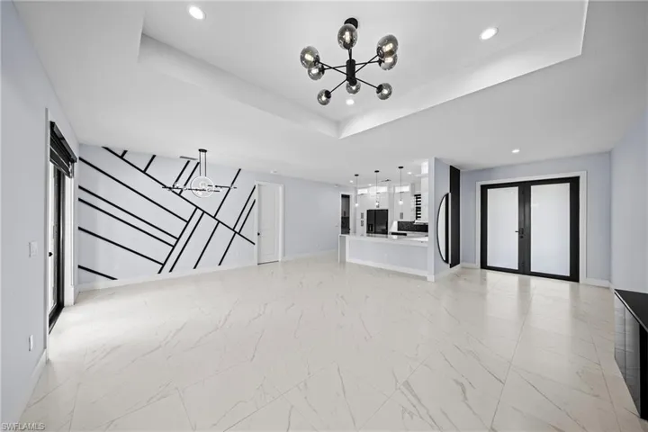 Unfurnished living room with a chandelier, recessed lighting, baseboards, a tray ceiling, and light marble finish floors