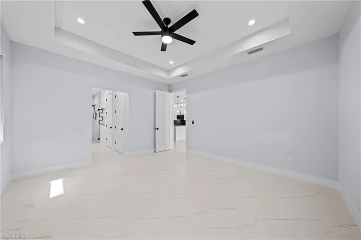 Spare room featuring a tray ceiling, ceiling fan, light marble finish flooring, baseboards, and recessed lighting