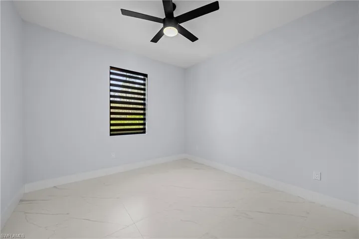 Spare room with marble look tiles, baseboards, and a ceiling fan