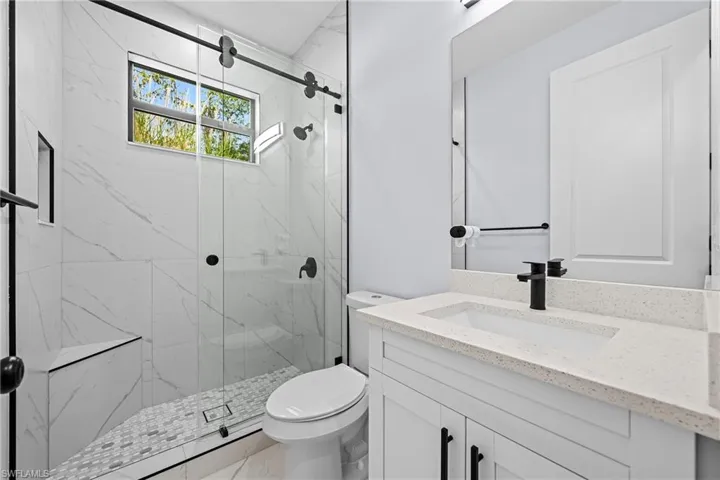 Full bath featuring vanity, a marble finish shower, toilet, and marble finish flooring