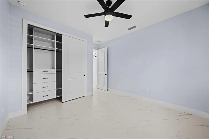 Unfurnished bedroom with baseboards, light marble finish floors, a closet, and a ceiling fan