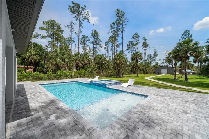 View of swimming pool with a patio, a yard, a pool with connected hot tub, and view of wooded area