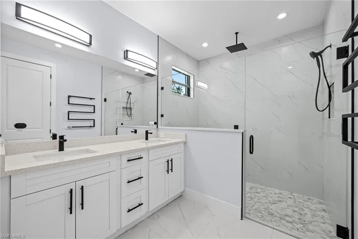 Bathroom with a marble finish shower, double vanity, marble look tile flooring, recessed lighting, and baseboards