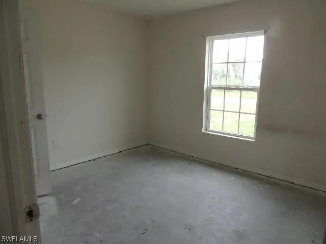 Spare room featuring unfinished concrete flooring and baseboards