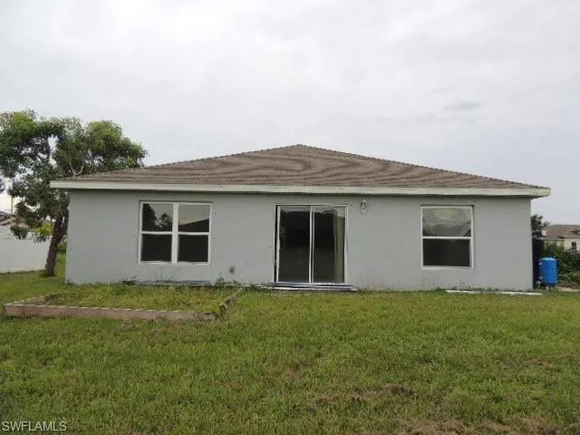 Back of house featuring a lawn and stucco siding