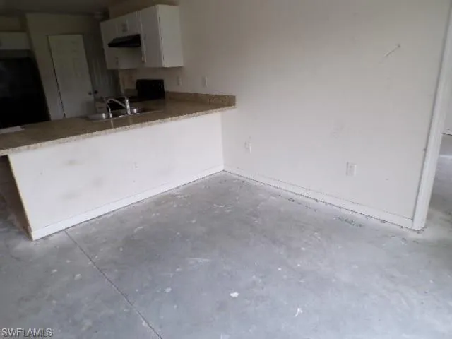 Kitchen with a peninsula, unfinished concrete flooring, white cabinetry, black range oven, and under cabinet range hood
