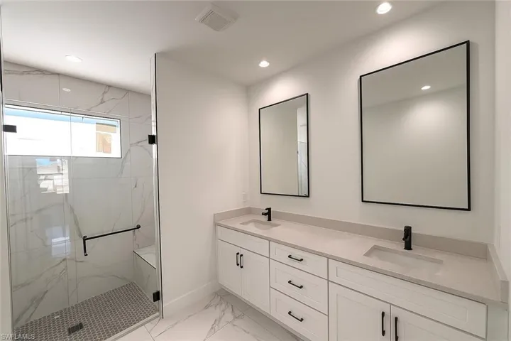 Bathroom featuring double vanity, light marble finish floors, a marble finish shower, and recessed lighting