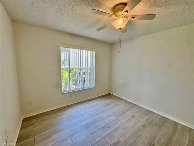 Room featuring wood-finish flooring, a ceiling fan with integrated lighting, and a window with vertical blinds