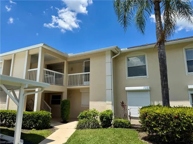 Two-story stucco exterior featuring multiple balconies with white railings, a covered carport, and a paver walkway
