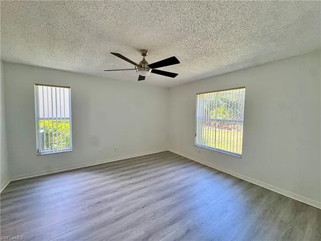 Spacious room featuring wood-finish flooring, two windows with vertical blinds, a ceiling fan with light fixture, and textured ceilings