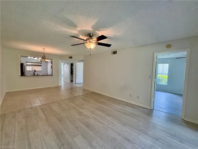 Bright living area featuring light-toned wood-finish flooring, a contemporary ceiling fan with integrated lighting, and a pass-through window to the kitchen