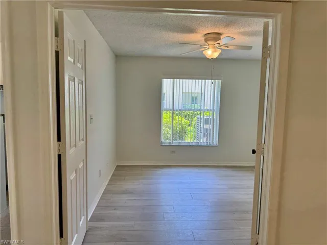 Room featuring wood-finish flooring, a window with vertical blinds, and a ceiling fan with integrated lighting
