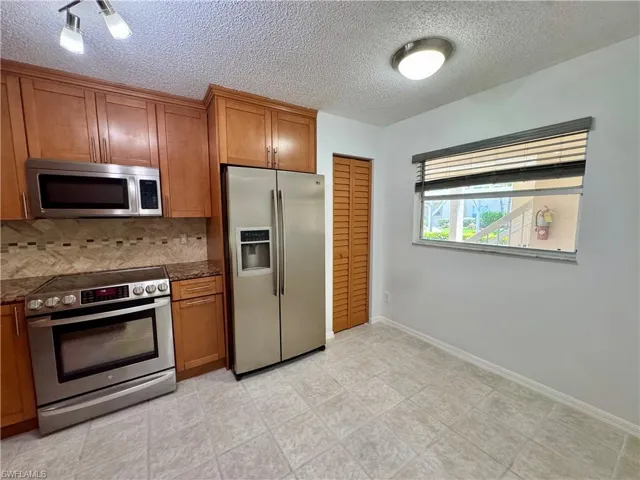 Kitchen featuring stainless steel appliances, wood cabinetry, patterned backsplash, and light-toned tile flooring
