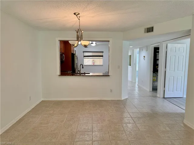 Tiled flooring throughout this open concept living area, featuring a decorative hanging light fixture, a pass-through window to the kitchen, and paneled interior doors