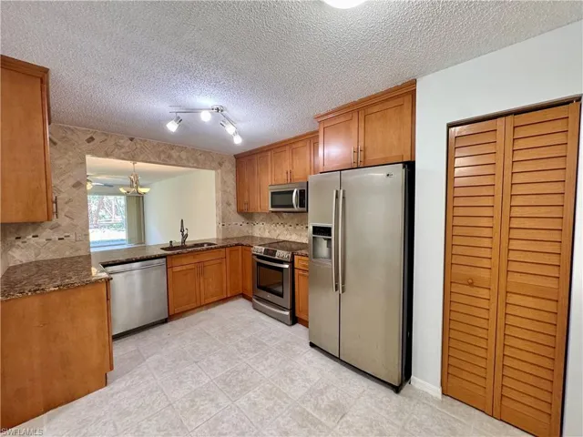 Kitchen featuring wood cabinetry, stainless steel appliances, granite countertops, and a tiled backsplash