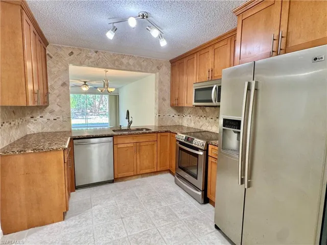 Kitchen featuring wood-finish cabinetry, stainless steel appliances, granite countertops, tile flooring, and a decorative tile backsplash