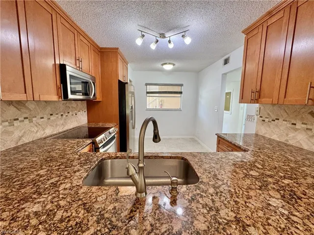 Kitchen featuring granite countertops, stainless steel undermount sink, brushed nickel faucet, wood cabinetry, and a patterned tile backsplash