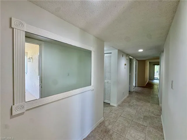 Hallway with tile flooring, recessed lighting, and a large wall-mounted mirror with decorative trim