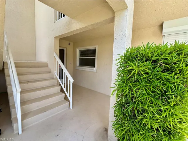 Exterior entry featuring a stucco finish, a covered walkway, and a white staircase with matching railings