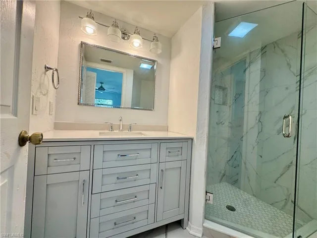Bathroom featuring a frameless glass shower enclosure, white marbled shower walls, and a light-toned vanity with a built-in sink