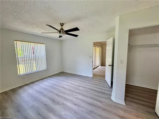 Spacious room featuring wood-finish flooring, a contemporary ceiling fan, and a wide window with vertical blinds